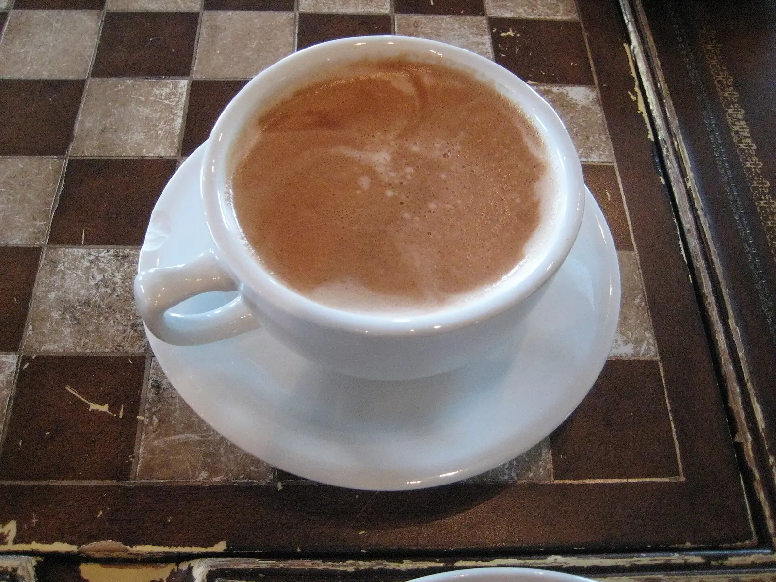 A mocha latte in a white cup on a checkerboard table at an Asheville cafe. The photo was not taken in Mooresville.