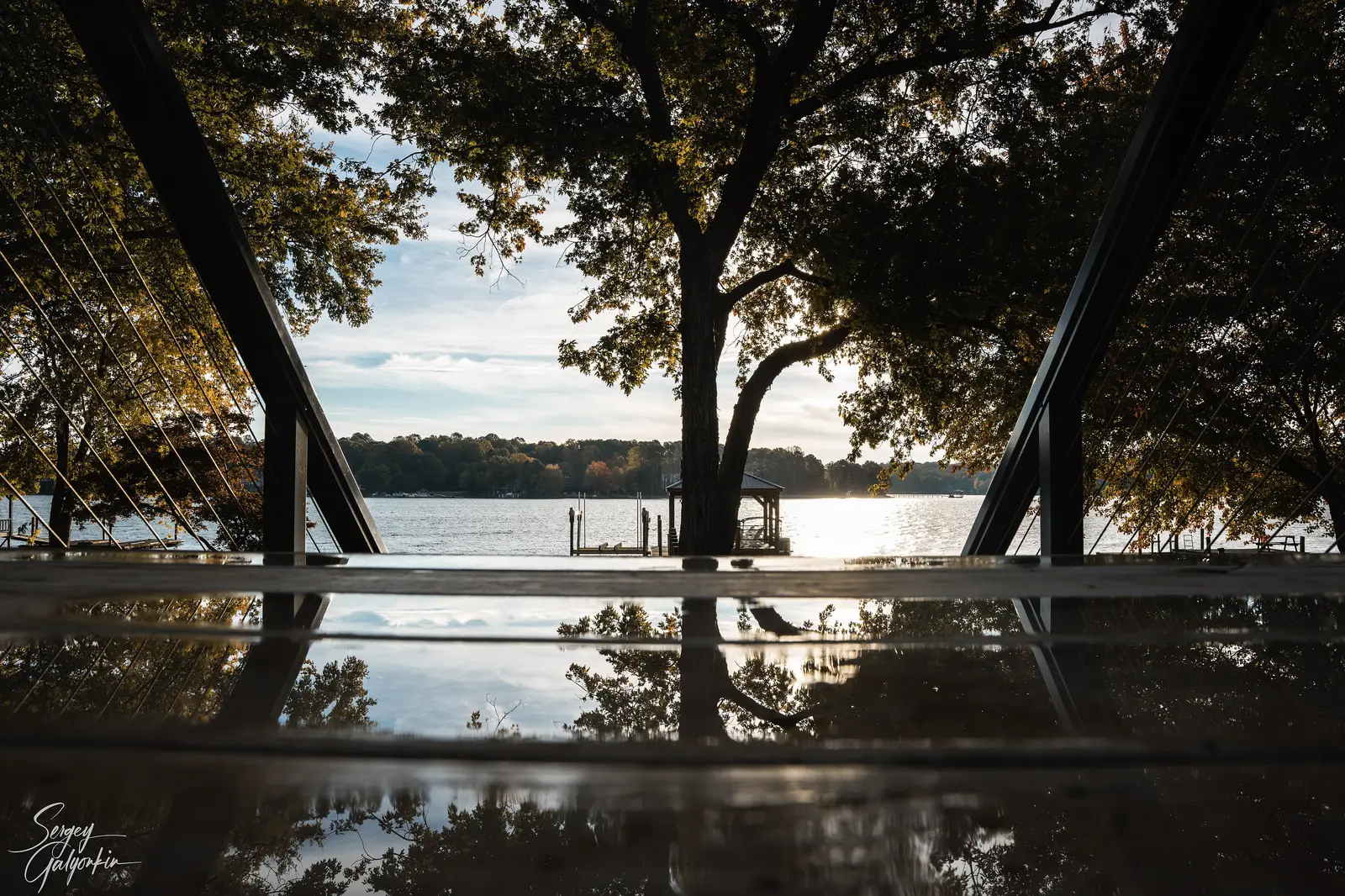 The sun sets over Lake Norman, seen through trees from a lakeside deck