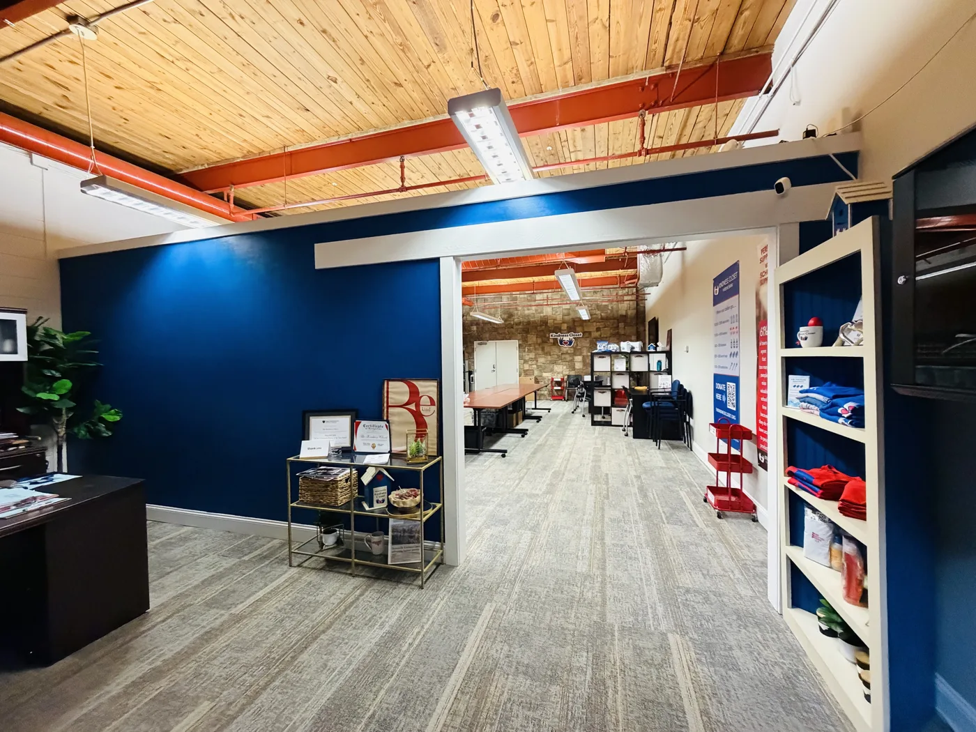 The Kindness Closet front office with a blue wall, gray carpet, display shelves and a doorway through to a work area