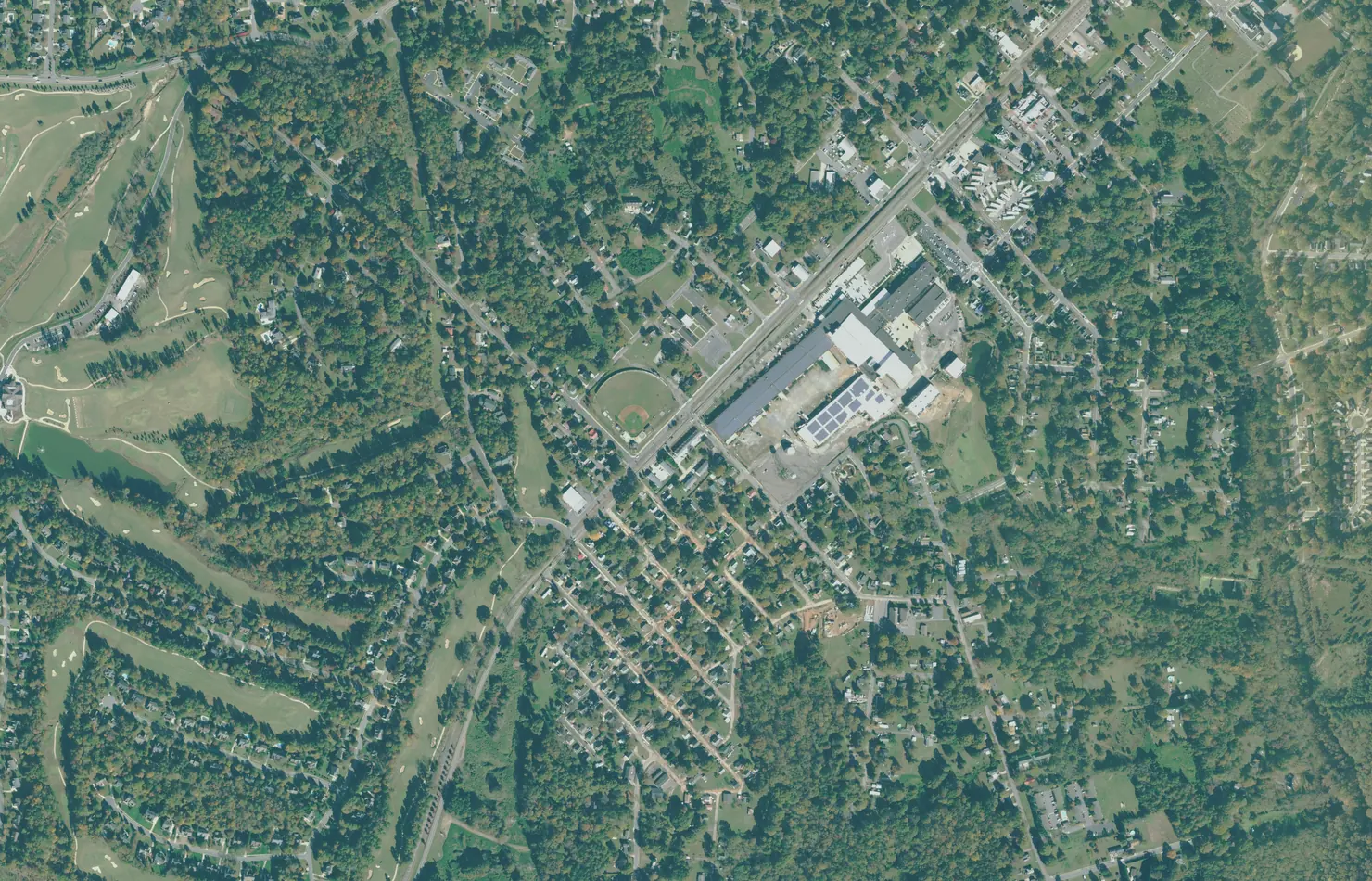 Aerial view of the Mooresville Mill Village, with the old cotton mill buildings and the railroad in the center, a ballfield beside them and the mill houses on the grid of streets to the south