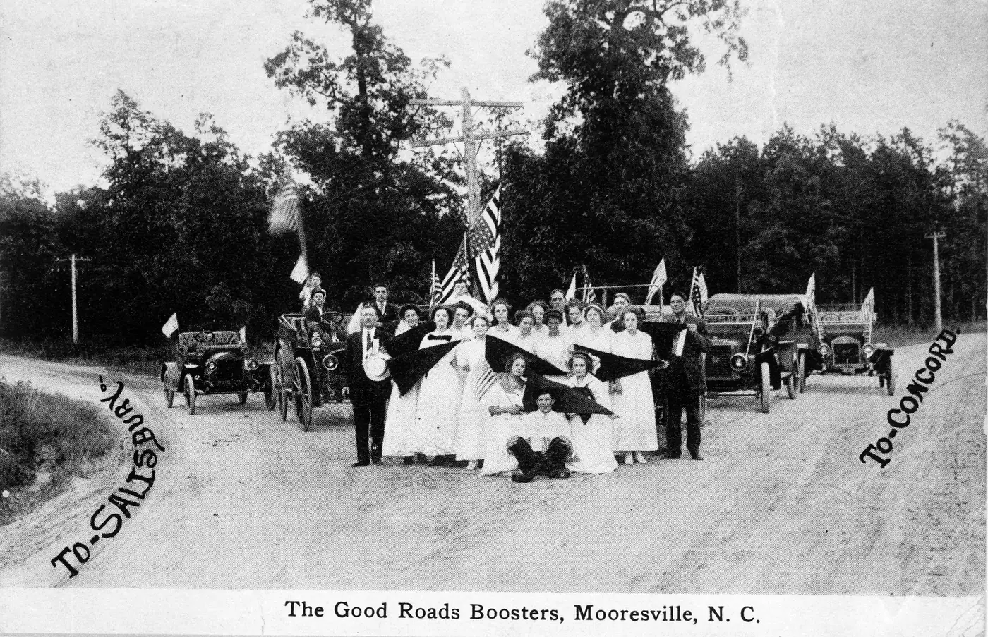 Members of Mooresville's Good Roads Boosters, a civic group, with banners and early automobiles at a fork in a town road around 1911